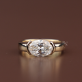 Close up view of a magnificent 3 carat oval cut lab grown diamond solitaire engagement ring set horizontally in an elegant 14k yellow gold east-west full bezel setting on a plain polished band.