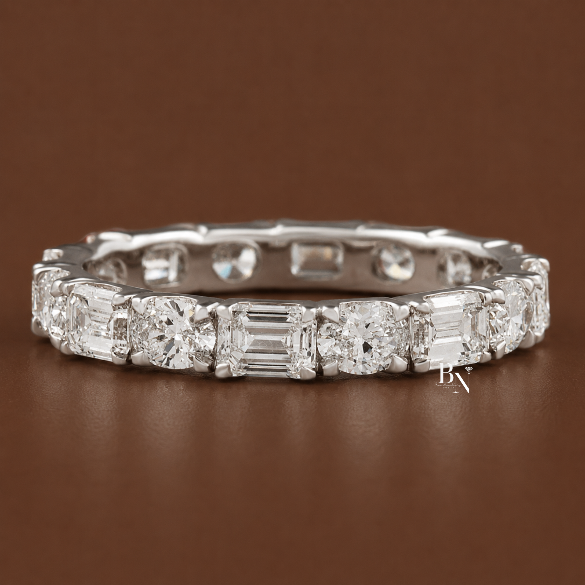 Alternating east-west oval and emerald cut lab diamond full eternity band in a u-shape prong setting. Showcasing 2 total carats on a 2.7mm 14K gold band, this luxury bridal stacking ring is displayed on-hand and in multiple gold tones.