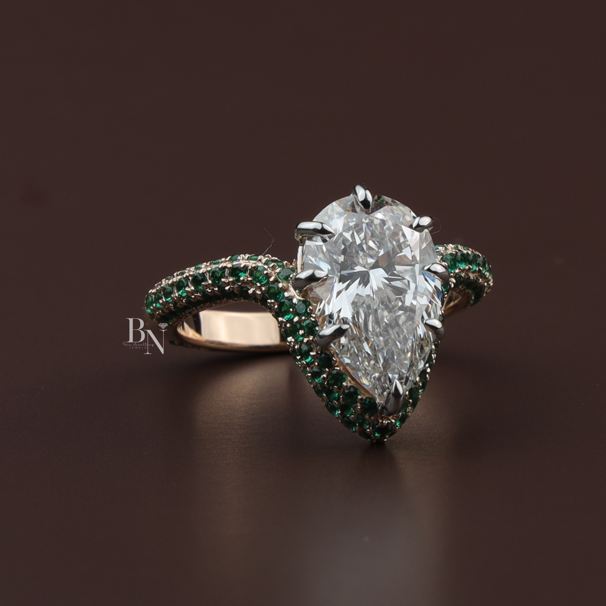 Pear cut lab diamond engagement ring with green gemstone halo and pavé-set emerald band in rose gold, luxury statement wedding ring.