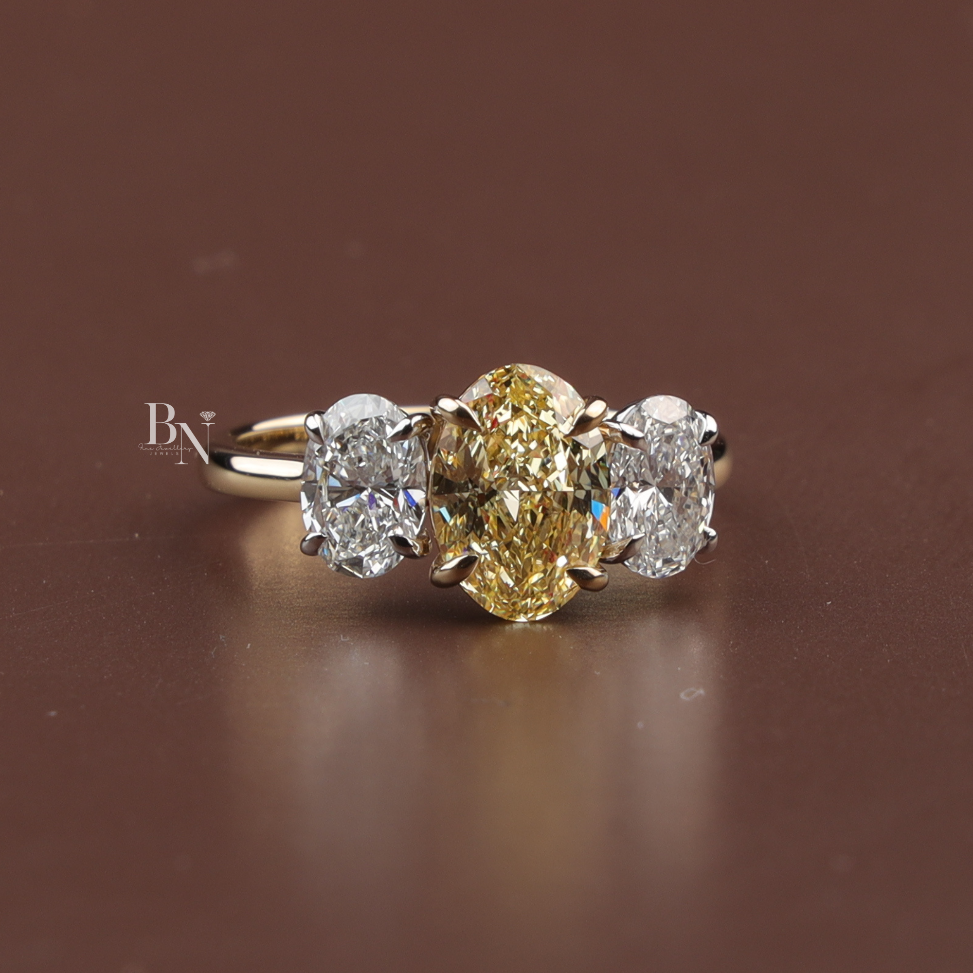 Fancy yellow oval lab diamond three stone ring set in 10k yellow gold, featuring two colorless side oval diamonds in a classic trilogy engagement setting.