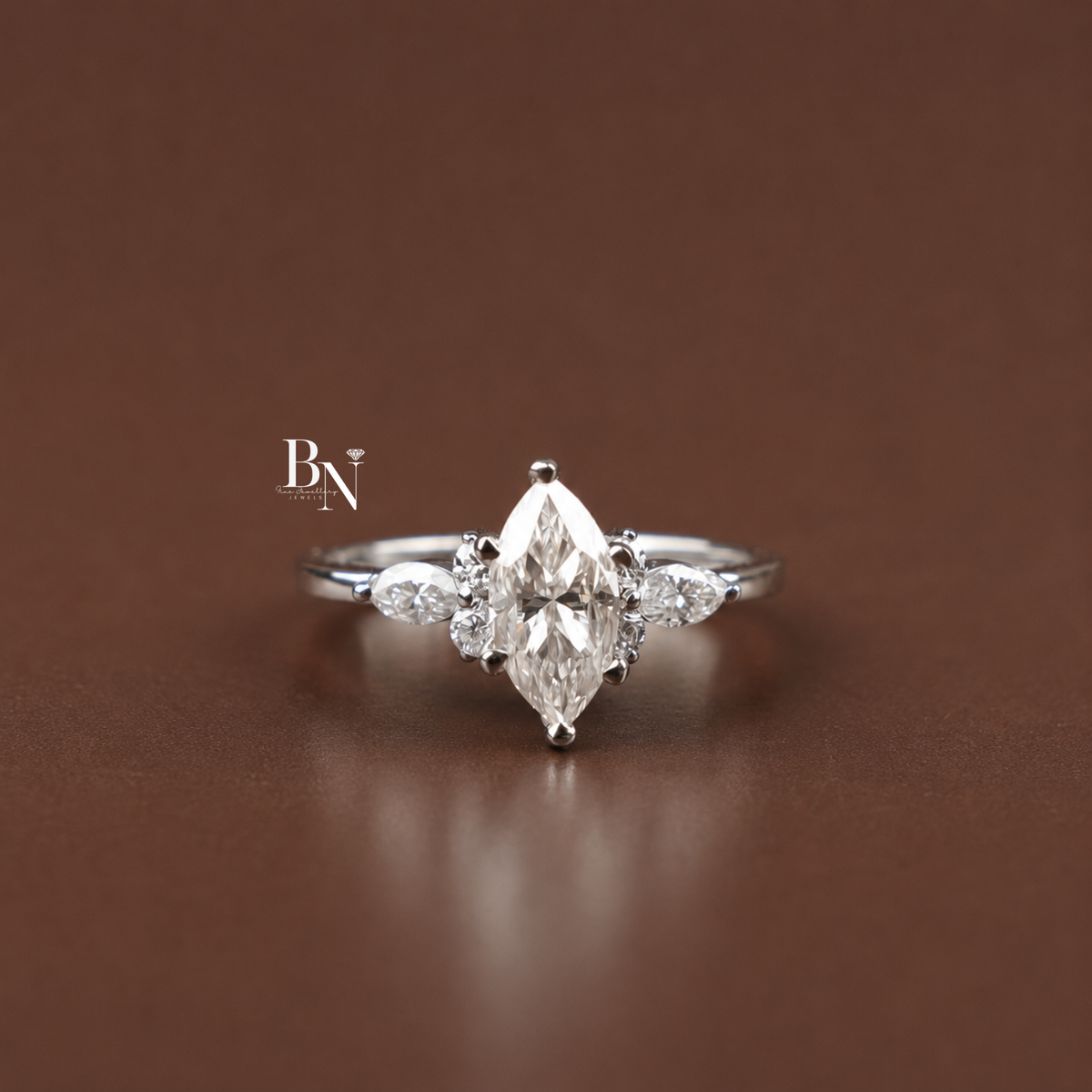 Front view of a marquise-cut engagement ring resting on a textured wooden surface, showcasing the center stone and asymmetrical cluster sides.