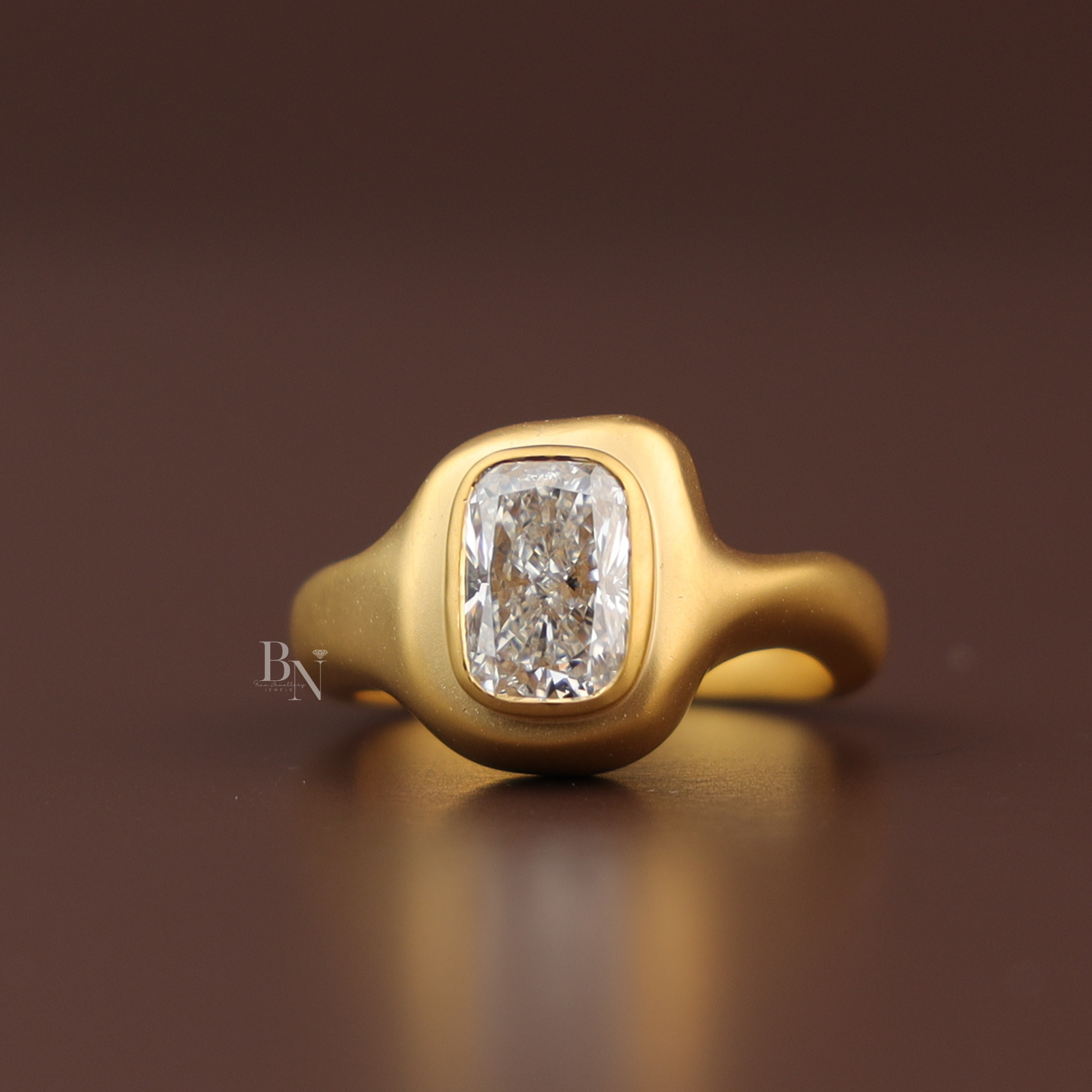 Sculptural 3 carat elongated cushion cut lab grown diamond engagement ring in matte brushed 14k yellow gold organic wide bezel setting worn on finger profile view showing smooth fluid modern craftsmanship.