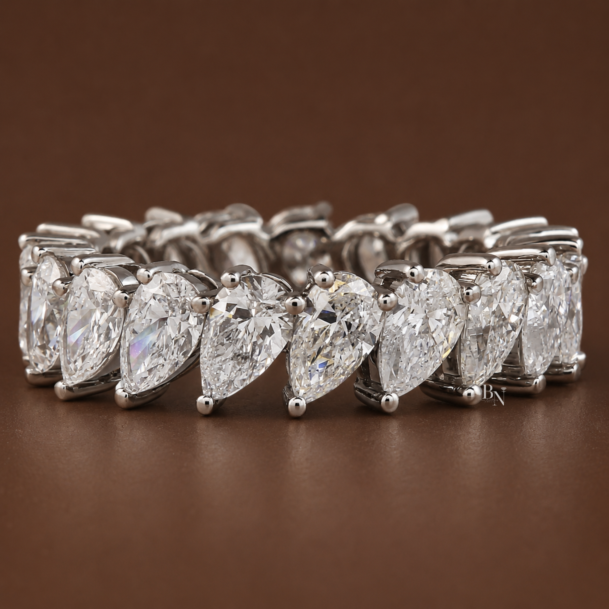 Angled front view of a platinum slanted pear diamond eternity band resting elegantly on a dark brown background.
