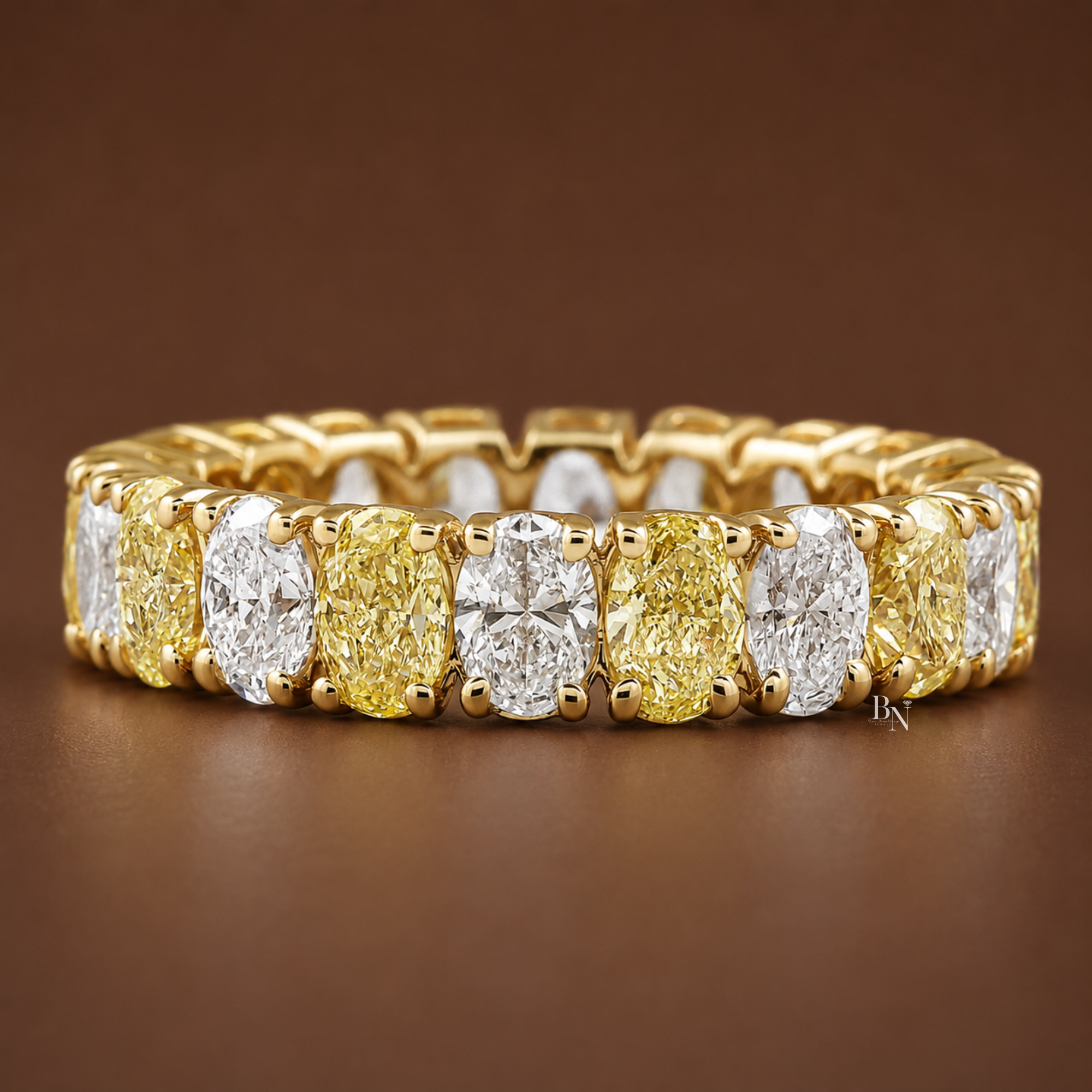Front angled view of the 14K yellow gold alternating oval diamond eternity band resting elegantly on a dark brown background.