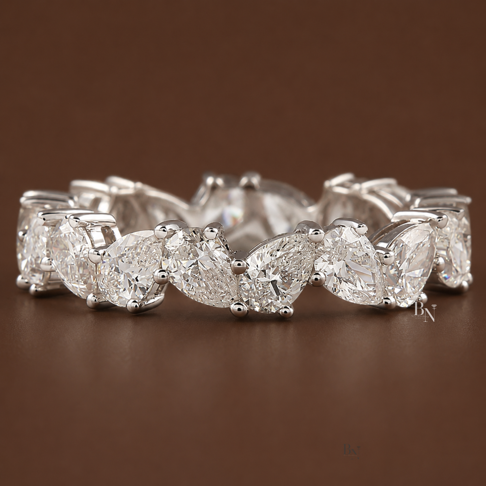 Angled front view of a 14K white gold eternity band featuring a zig-zag arrangement of pear-shaped lab diamonds on a brown background.