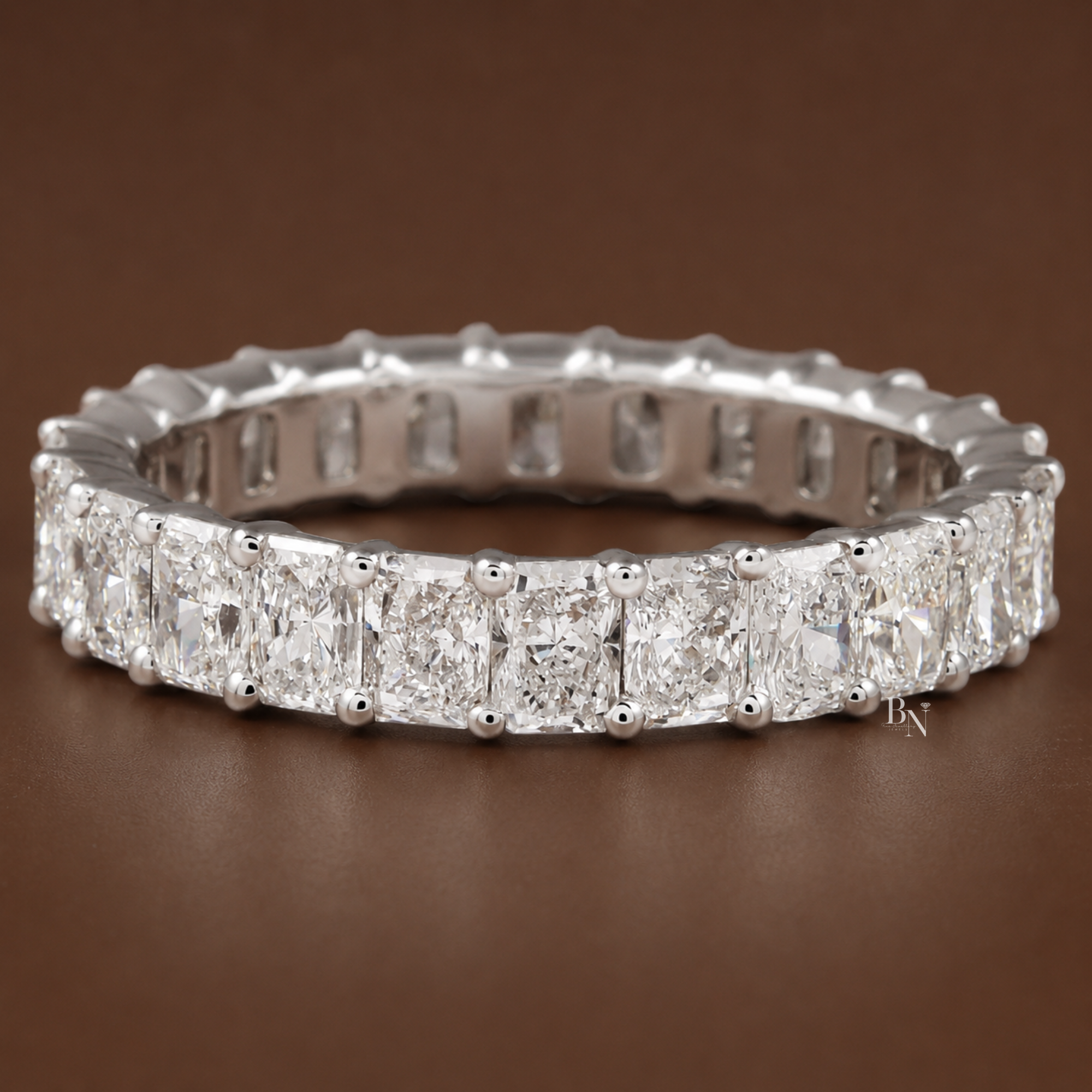 Finger modeling four different radiant-cut diamond eternity bands of varying widths to demonstrate scale and proportion.