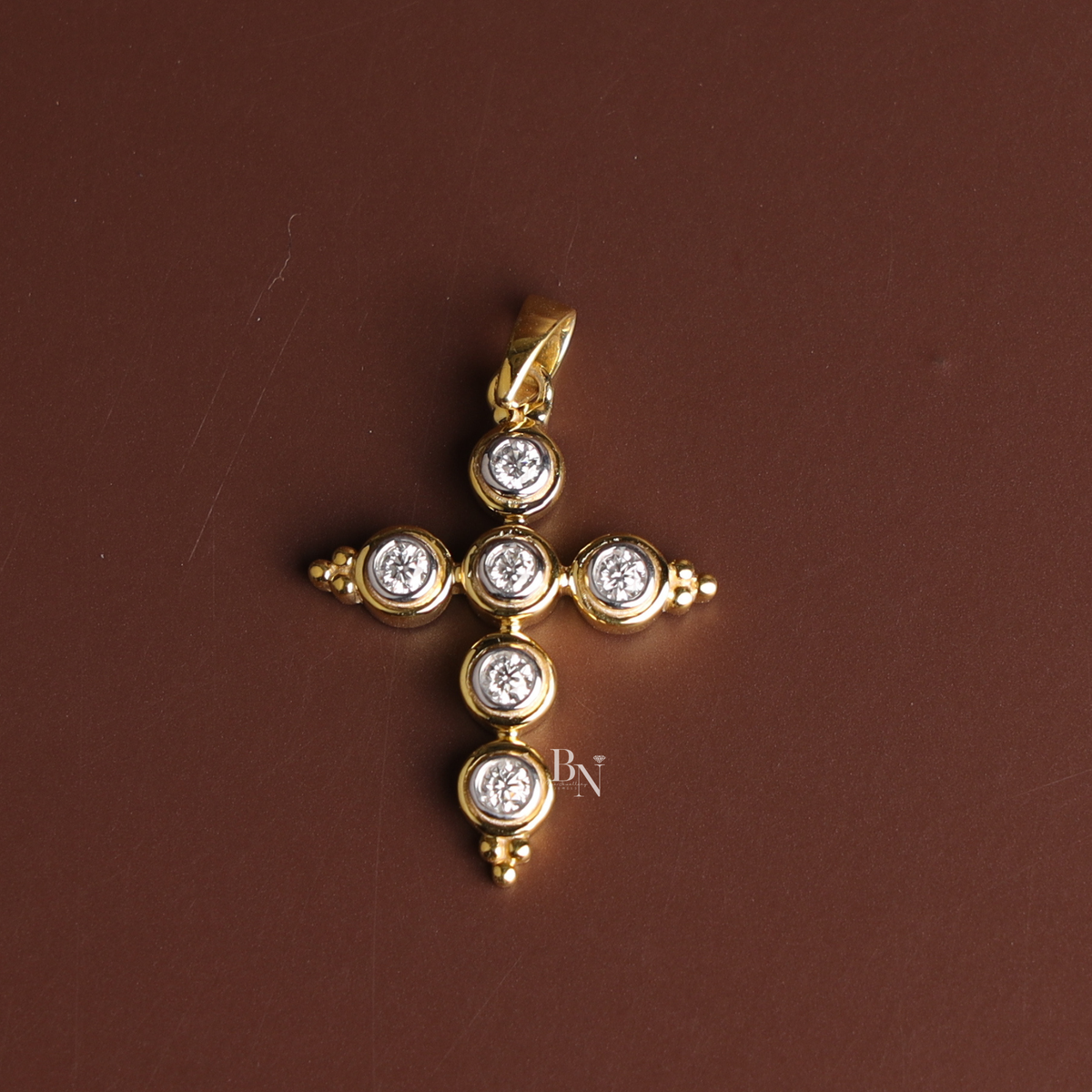 A woman's chest wearing a dainty yellow gold-tone cross necklace featuring six bezel-set round lab-grown diamonds on a delicate cable chain.