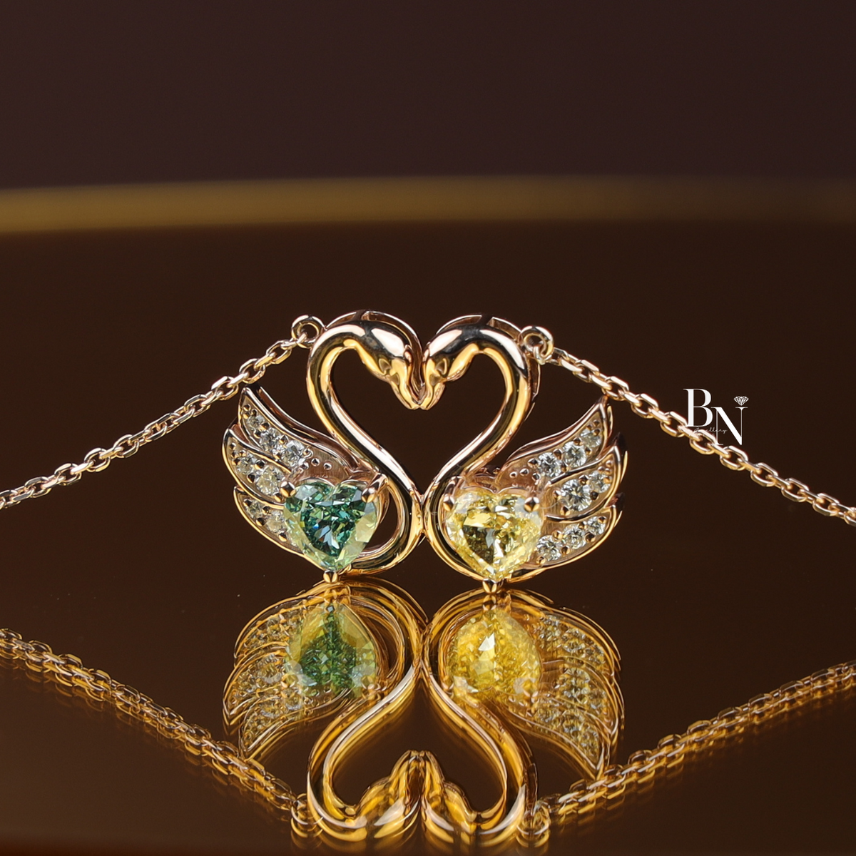 Front view of an interlocking dual swan pendant necklace in polished white metal holding a 1ct heart-cut fancy green lab diamond and a 1ct heart-cut fancy yellow lab diamond with pavé diamond wings on a fine cable chain.