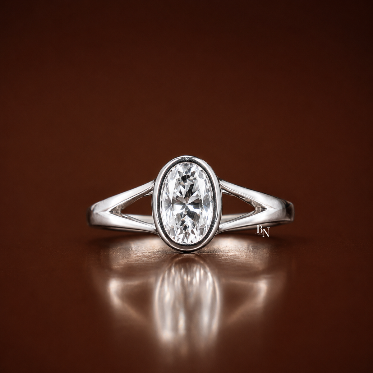 Front view of a white gold tone solitaire ring featuring a 1 carat oval lab-grown diamond held in a full bezel setting with split shank shoulders, resting on a rustic wood block.