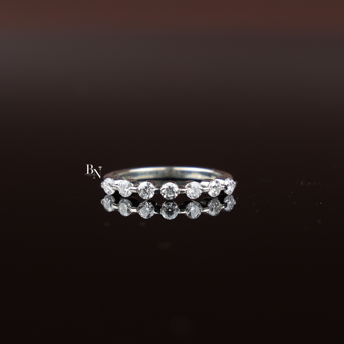 Slim white gold tone ring featuring a row of round lab grown diamonds worn on a human hand against a brown background.