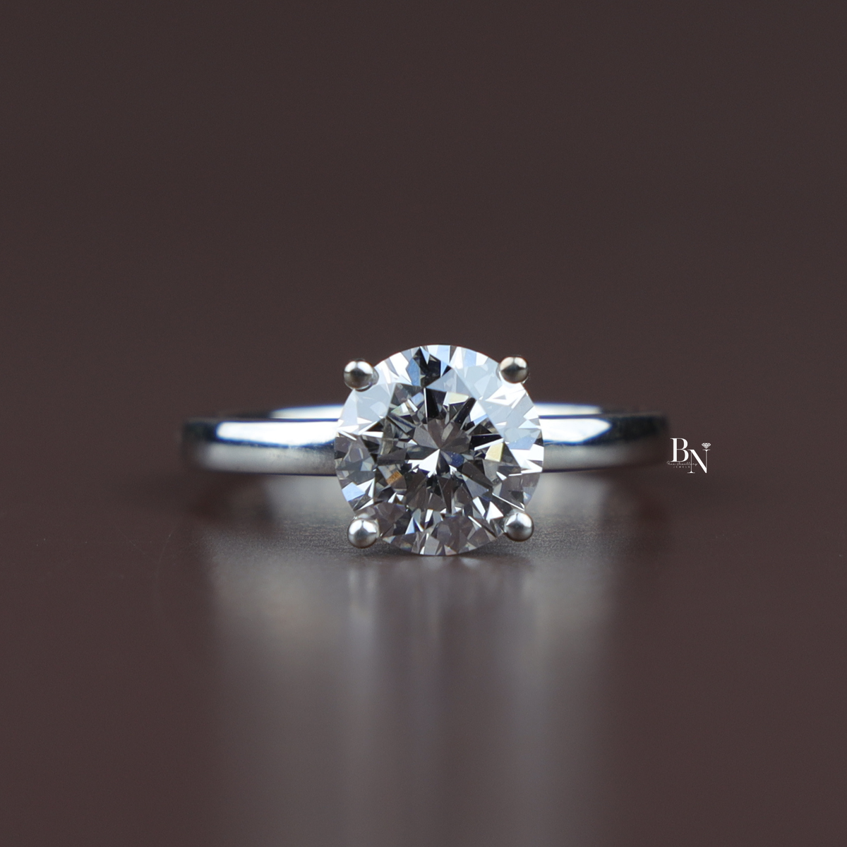 On-hand view of a 2 carat round cut lab grown diamond solitaire engagement ring featuring a silver-tone plain band and a four-prong setting.