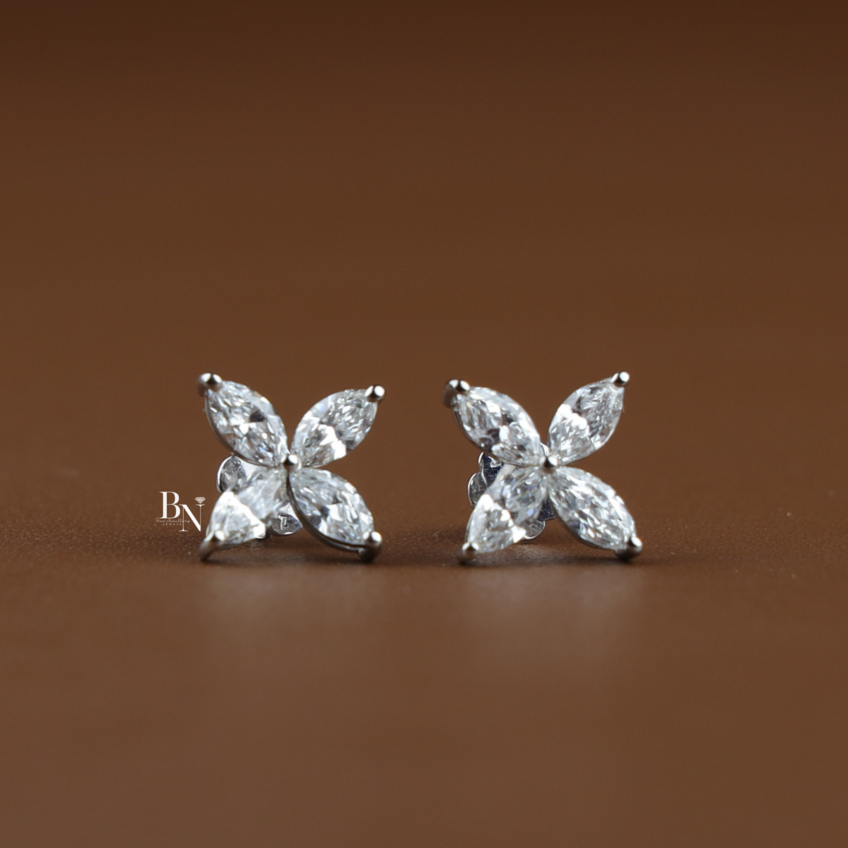 Pair of white metal stud earrings featuring four marquise cut lab grown diamonds arranged in a flower cluster on wood slice.