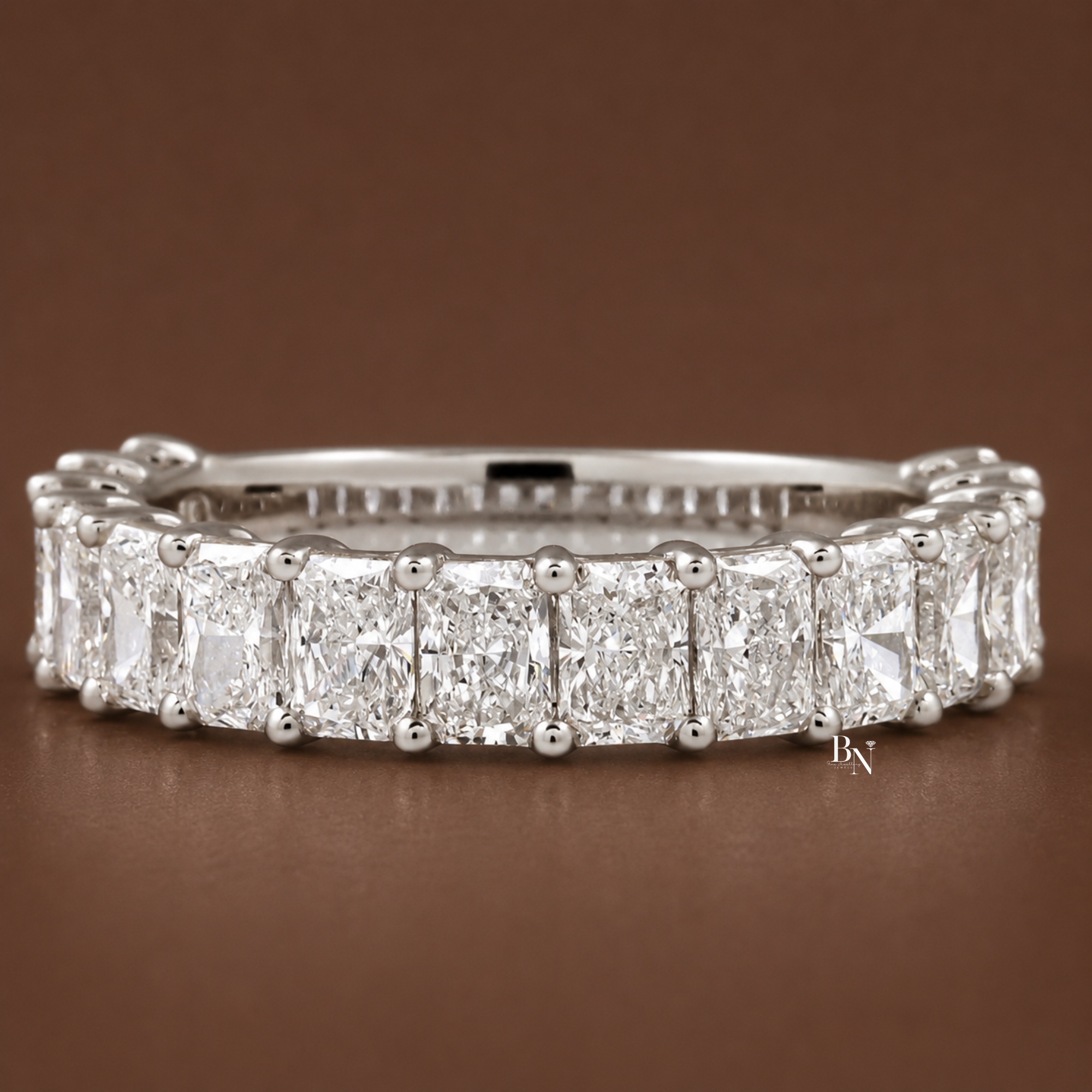 Front angled view of a white gold radiant cut lab diamond band resting gracefully on a warm brown background.