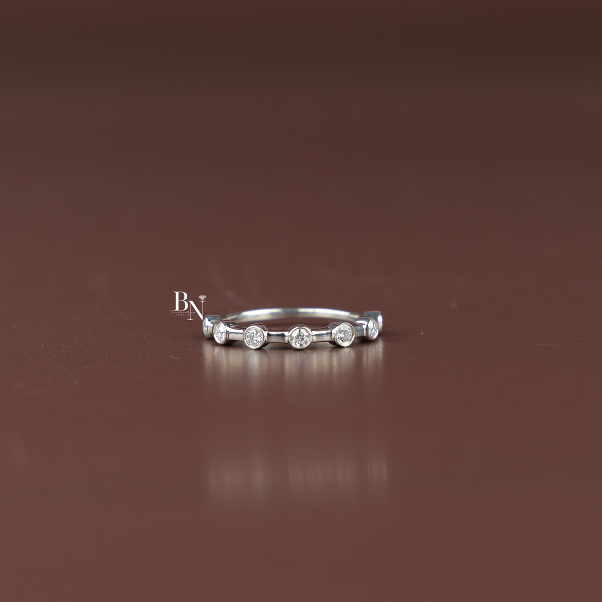 Delicate white metal ring featuring spaced round lab-grown diamonds in bezel settings, captured in a clean front studio view.