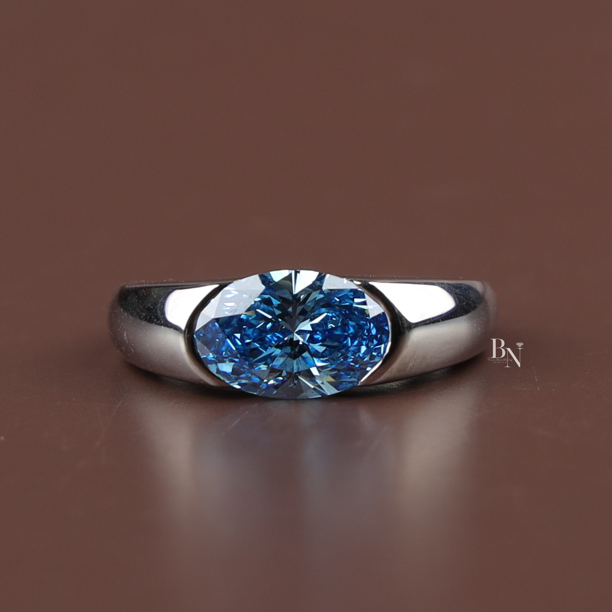 Front-facing view of a modern white metal cocktail ring featuring a prominent 2 ct fancy blue oval-cut lab-grown diamond in a sleek bezel setting.