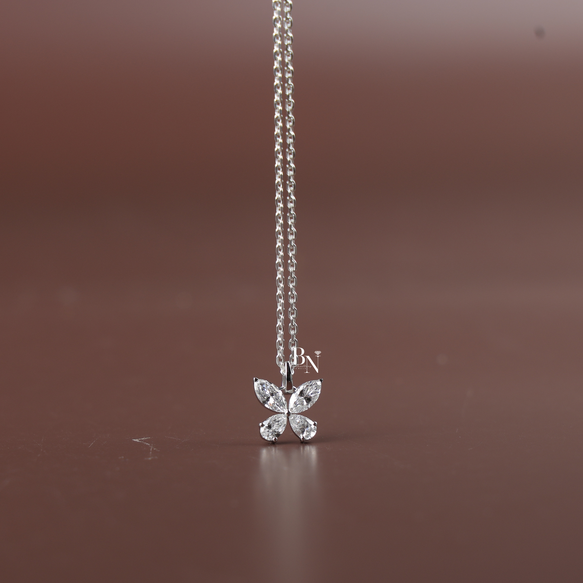 Close-up shot of a delicate white gold tone butterfly pendant necklace resting on a person wearing a black top, featuring marquise and pear cut lab-grown diamond wings.