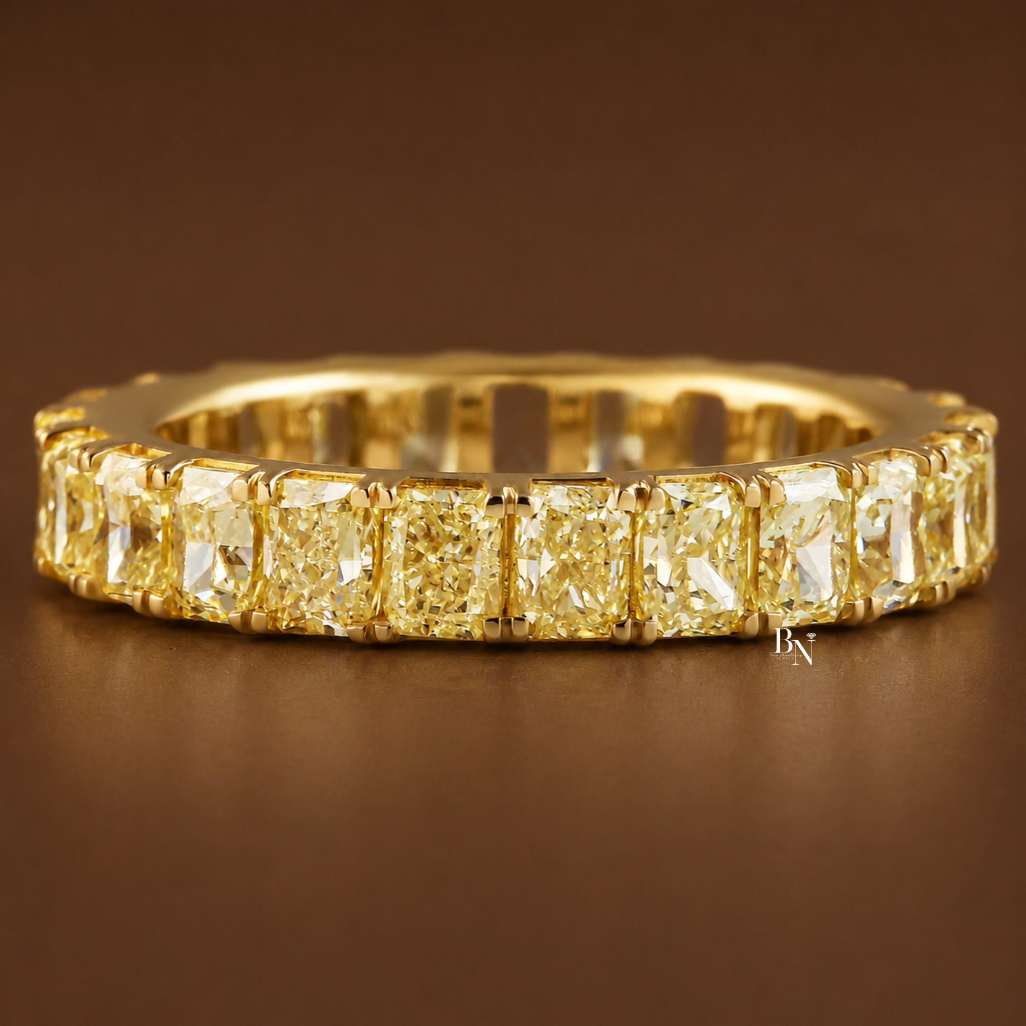 Front angled view of a yellow gold eternity band featuring vivid fancy yellow radiant cut lab diamonds resting on a warm brown background.