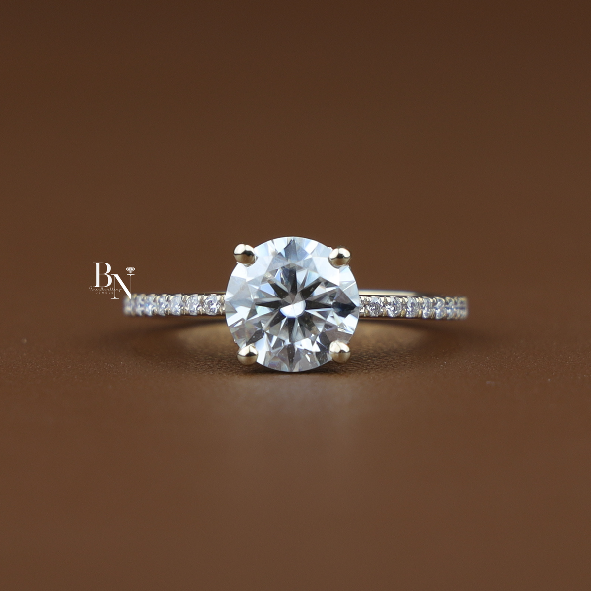 Angled front view of a 2 carat round lab-grown diamond engagement ring with a hidden halo setting and pavé diamond band resting on a brown surface.