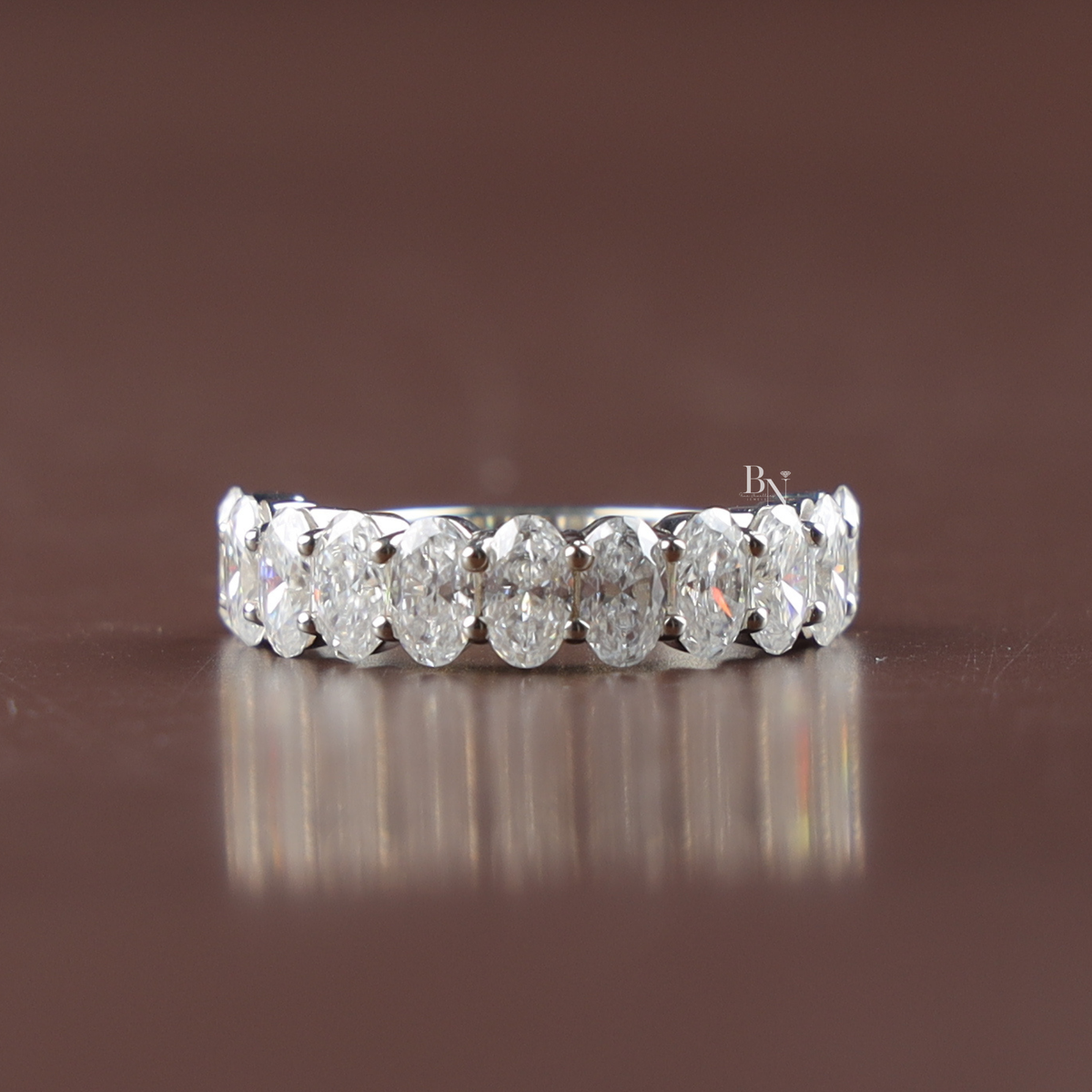 A 2.3ct lab-grown diamond half-eternity band featuring oval-cut stones in a silver-tone shared-prong setting, resting on a black reflective surface.