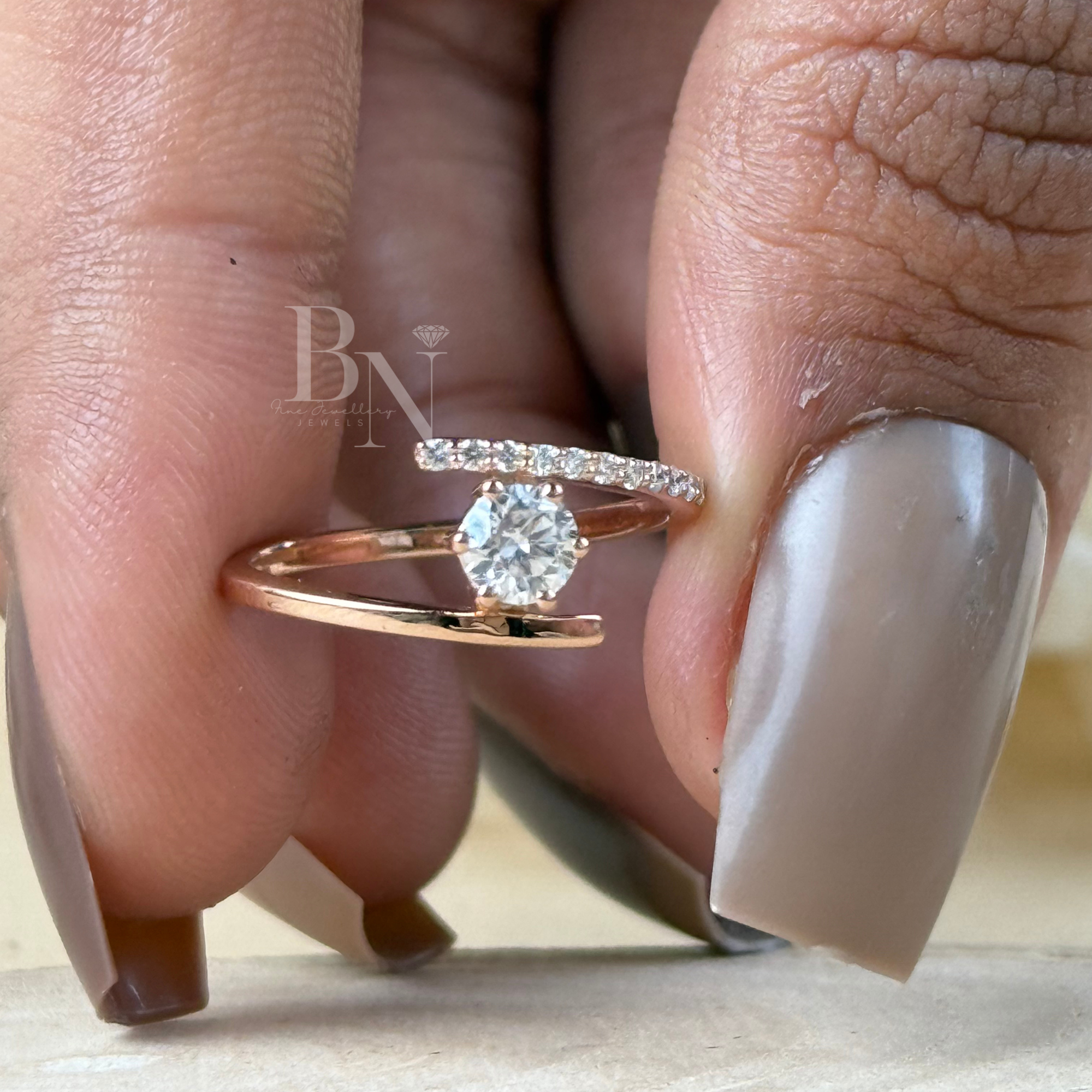 Minimalist bypass engagement ring in 14k rose gold featuring a 0.25 carat round brilliant lab grown diamond in a floating tension setting with one pave diamond side and one polished gold side.