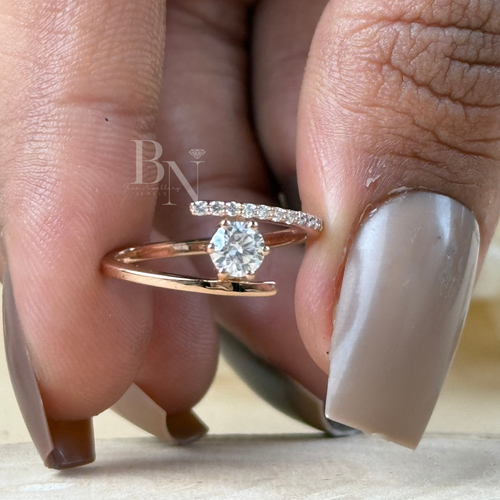 Minimalist bypass engagement ring in 14k rose gold featuring a 0.25 carat round brilliant lab grown diamond in a floating tension setting with one pave diamond side and one polished gold side.