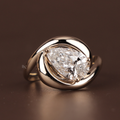 A 3.00 carat teardrop pear cut lab grown diamond set in a high-polish 14k gold swirl bypass solitaire setting, shown on a finger and reflecting on a mirror surface.