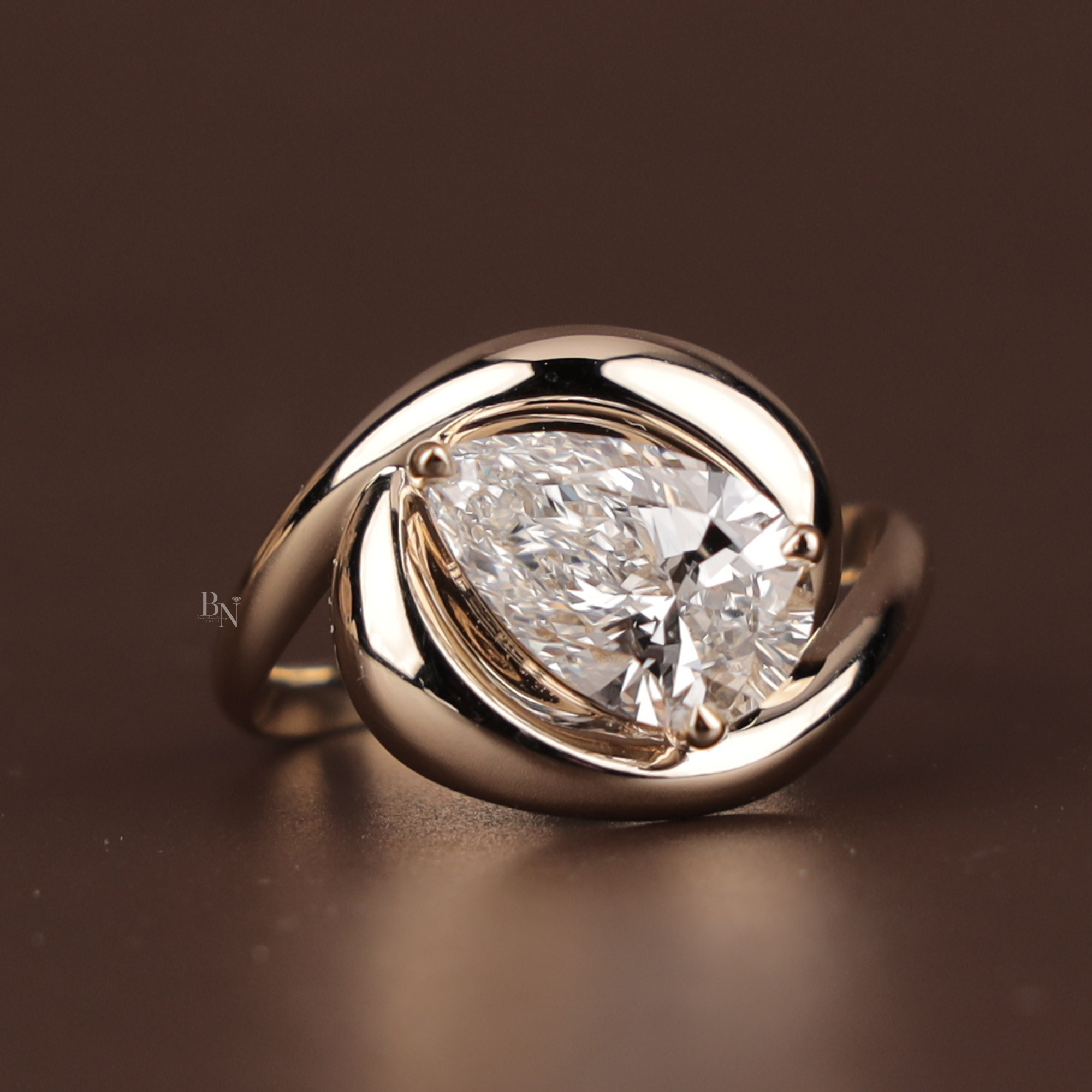 A 3.00 carat teardrop pear cut lab grown diamond set in a high-polish 14k gold swirl bypass solitaire setting, shown on a finger and reflecting on a mirror surface.