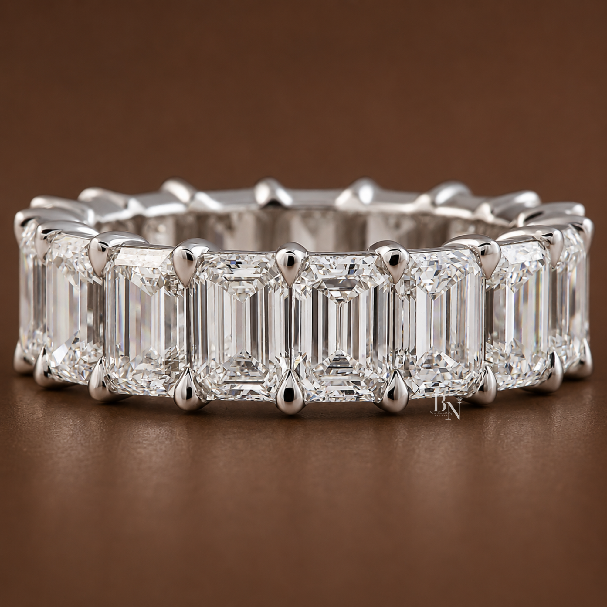 Front view of an eternity band with large emerald-cut lab diamonds set in a highly polished white metal closed-basket setting against a brown background.