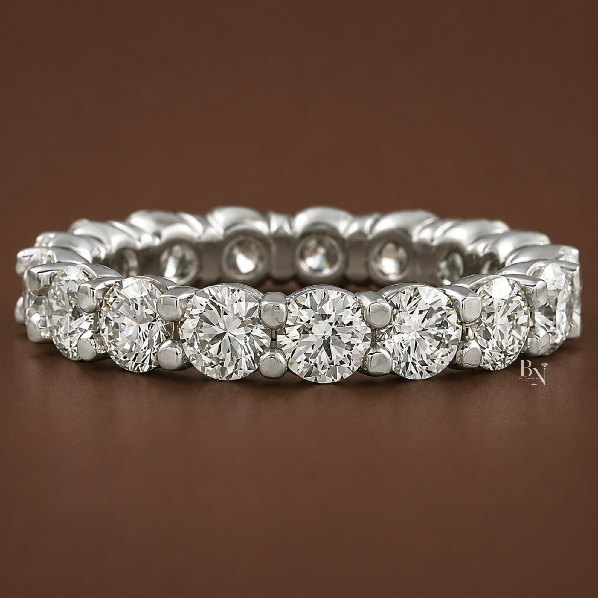 Angled front view of a white metal shared-prong round diamond eternity band resting on a dark brown background.