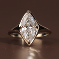 Top and profile view of an elongated marquise cut lab grown diamond in a sculptural 14k yellow gold bezel setting with integrated V-prongs, showing a polished seamless band and high-clarity Type IIa diamond brilliance.