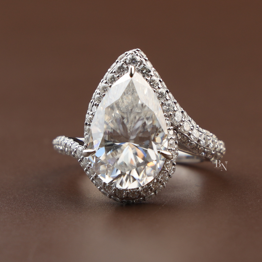 Stunning 5.50ct pear moissanite bypass ring in 14k white gold highlighting the intense rainbow fire and disco ball effect of the double tiered halo and shimmering triple-row pavé shank on a model's hand.