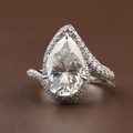 Stunning 5.50ct pear moissanite bypass ring in 14k white gold highlighting the intense rainbow fire and disco ball effect of the double tiered halo and shimmering triple-row pavé shank on a model's hand.
