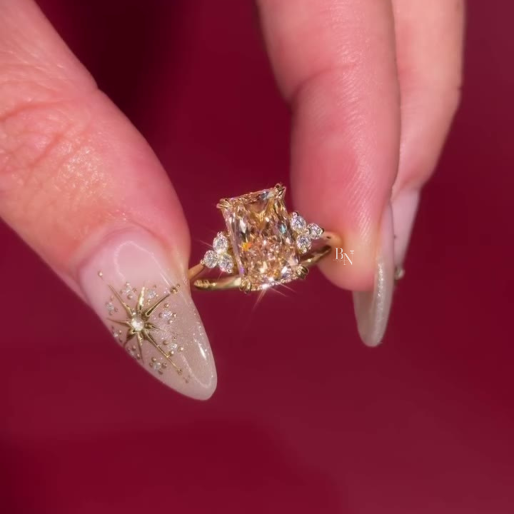 Handheld view of a 3 carat fancy yellow radiant cut lab grown diamond engagement ring in 14k yellow gold featuring a hidden halo setting and brilliant trillion-shaped diamond side clusters on a dainty gold band.