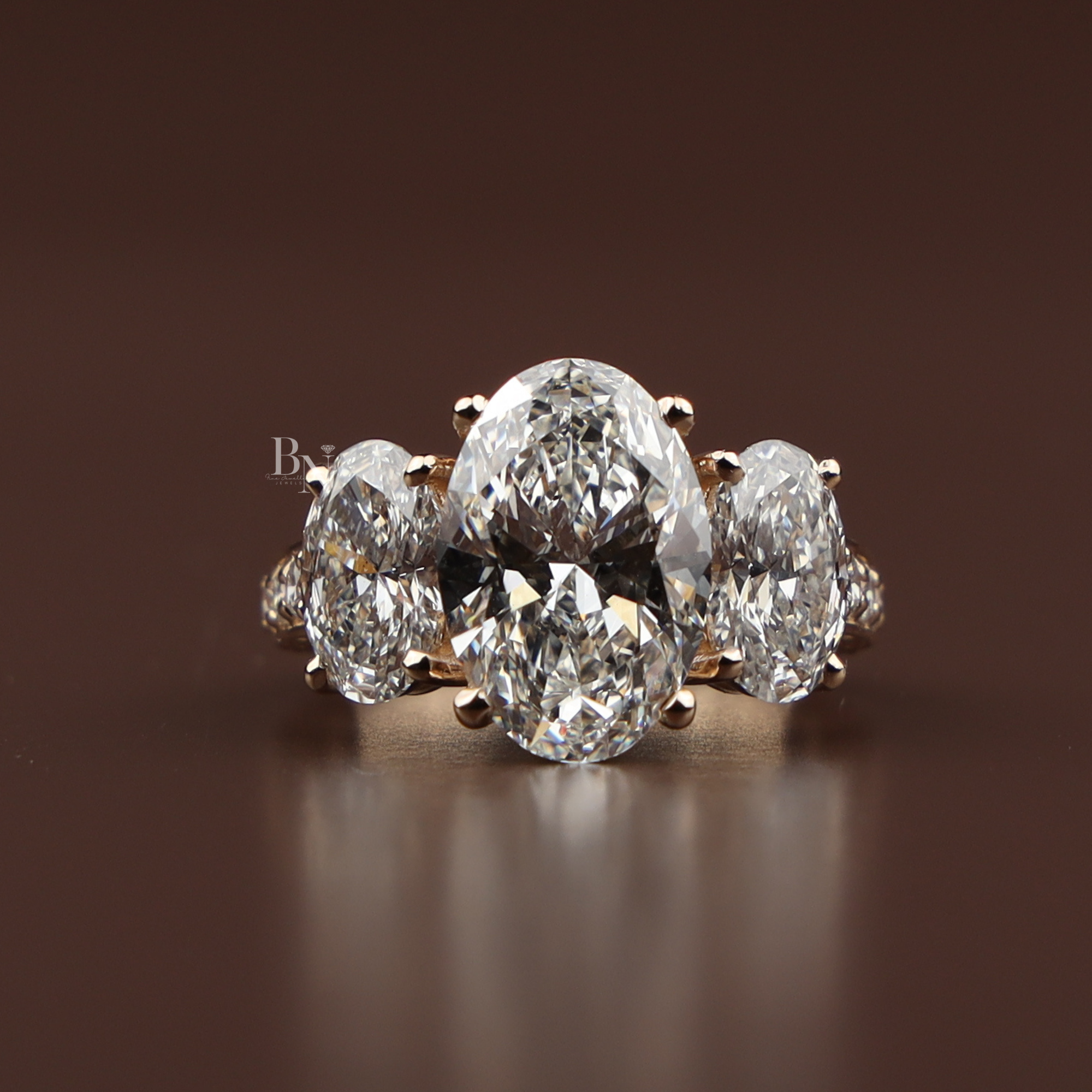A 4 carat graduated three stone oval lab grown diamond engagement ring crafted in solid rose gold featuring sparkling pave diamond accents on the band shown from the front side profile and on a hand.