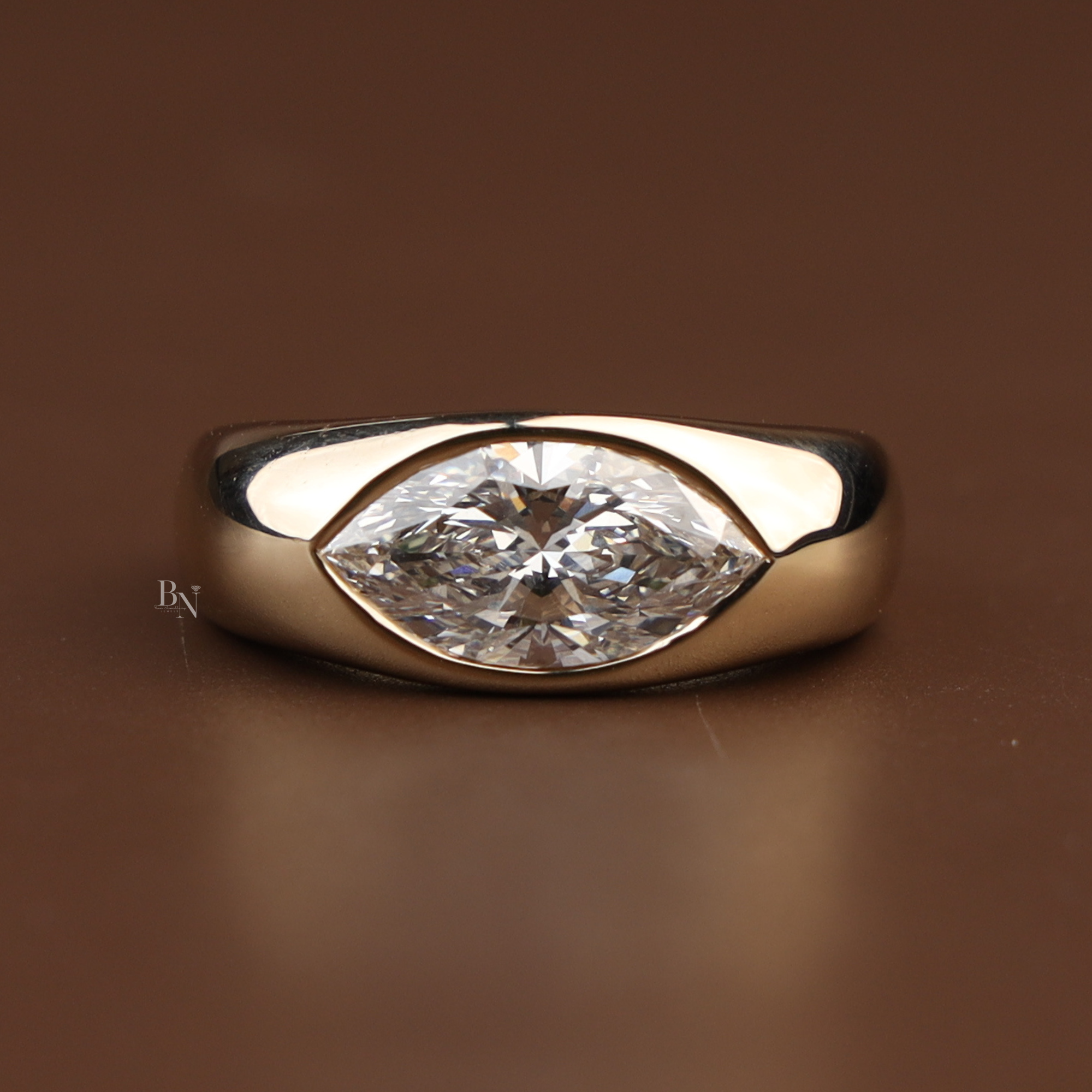 1.50 carat marquise brilliant lab grown diamond set horizontally in a protective 14k yellow gold bezel setting with a thick, high-polished wide cigar band showing modern minimalist luxury and ethical craftsmanship.