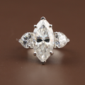 5.50 carat marquise cut lab grown diamond three stone engagement ring with heart shaped side diamonds in 14k white gold showing V-tip prongs and brilliant scintillation.