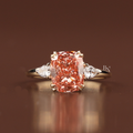 A 3 carat fancy pink cushion cut lab grown diamond engagement ring in yellow gold featuring pear shaped white diamond side accents and a double claw prong setting shown from multiple side angles and worn on a finger.