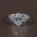 Hand view of 2 carat oval cut lab grown diamond engagement ring in 14k white gold featuring a brilliant center stone and unique floral cluster side diamonds on a thin polished band for a modern bridal look.