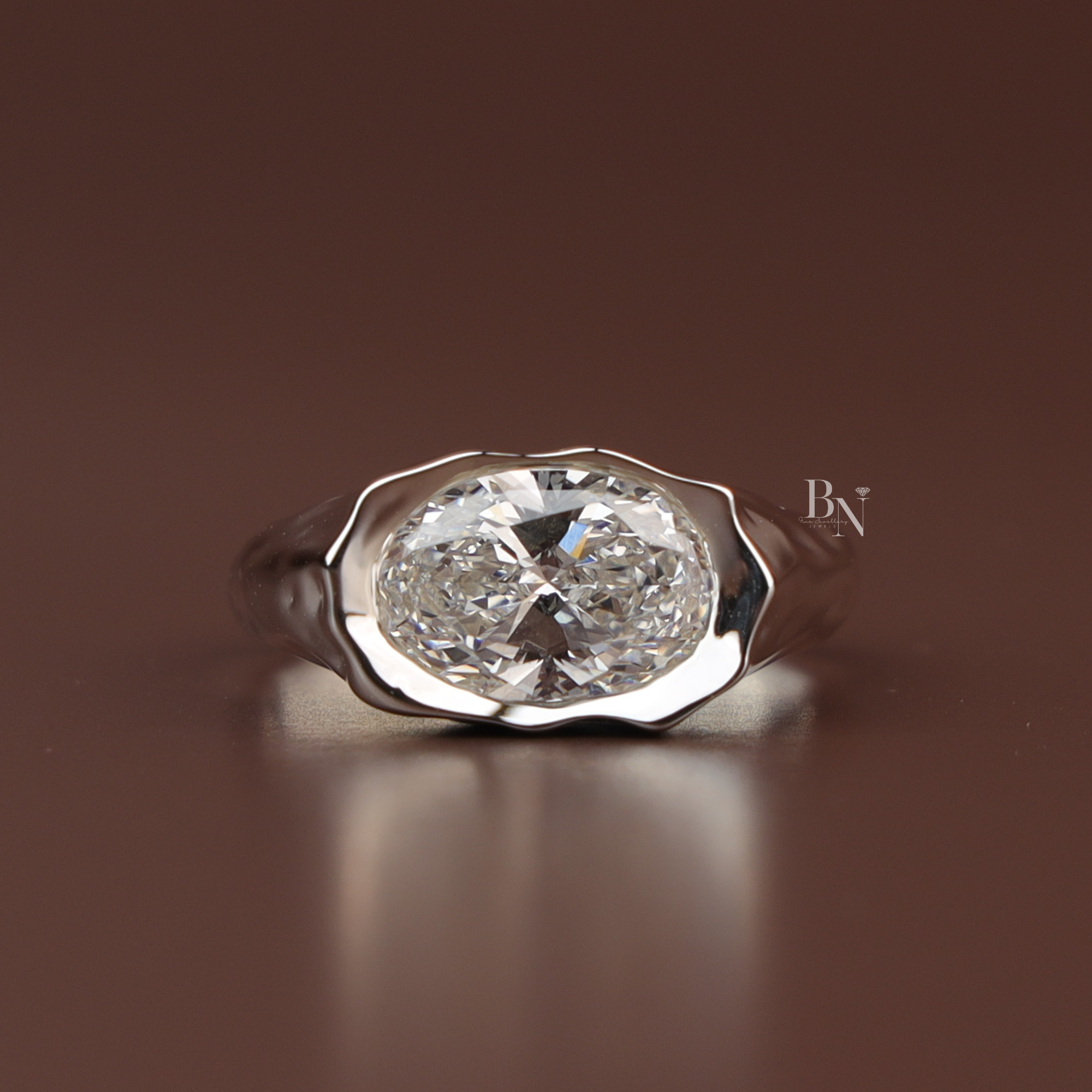 Three carat oval lab grown diamond engagement ring in a heavy platinum molten metal signet setting featuring an east west oriented fluid wavy bezel band design shown from the top profile and inside a black ring box.