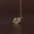 Brilliant cut six carat fancy yellow oval moissanite solitaire pendant necklace displaying exceptional fire set in 14k yellow gold claws on a delicate cable chain shown close up on a model.