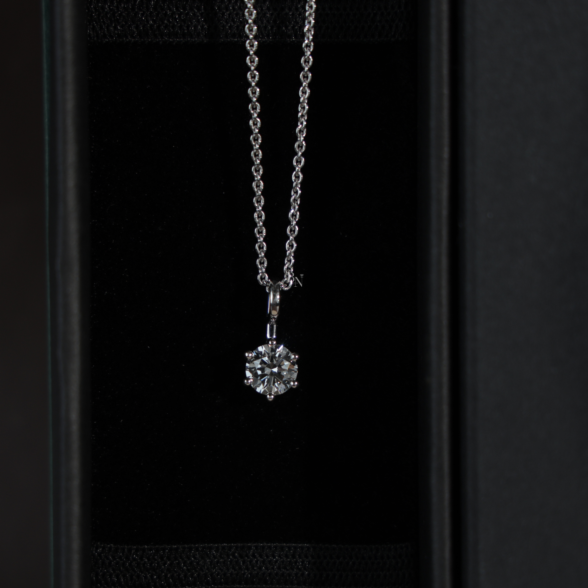 Macro view of a round brilliant cut lab grown diamond solitaire pendant in a 6-prong 14k white gold setting, hanging from a dainty cable chain, showcasing high clarity and crisp white light brilliance.