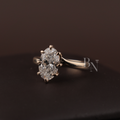 May include: A gold engagement ring featuring a large, clear gemstone. The ring is displayed on a wooden surface, highlighting its design. The band is polished gold, and the gemstone is secured by prongs. A classic piece of jewellery.