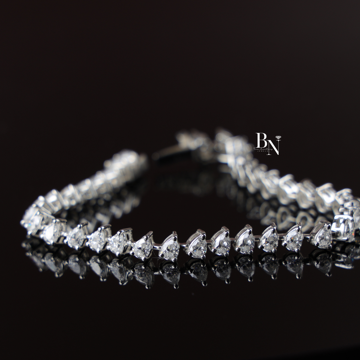 A 5.50 carat pear-cut lab-grown diamond tennis bracelet set in white metal resting on a natural wood slice.