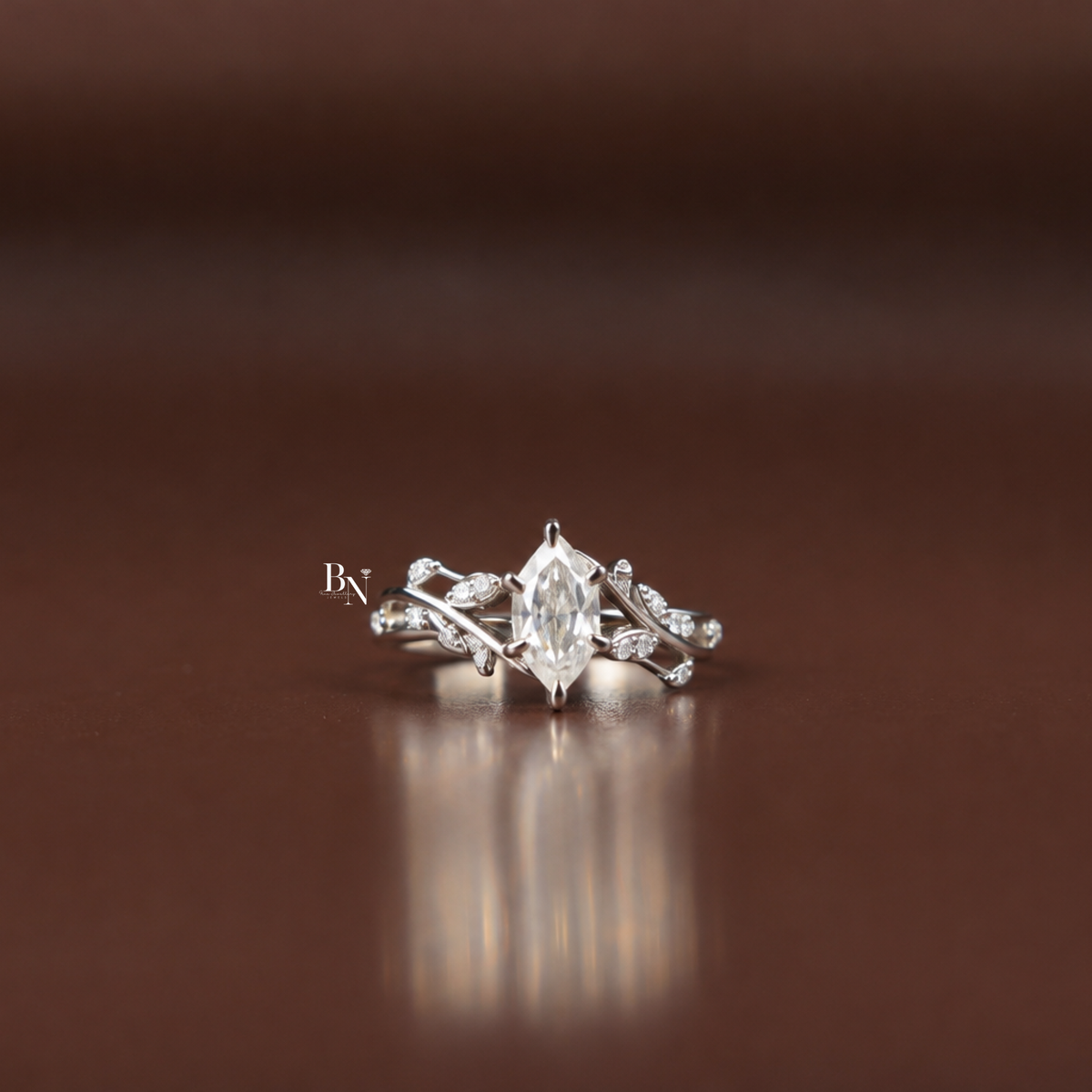 1 carat Dutch marquise-cut lab-grown diamond engagement ring featuring an intricate vine and leaf design band in white metal, set on a natural wood slice.