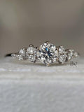 A woman's hand wearing a delicate 0.50 carat round lab diamond cluster ring. The asymmetrical design with multiple small IGI certified diamonds sparkles on a thin white gold band, showcasing its unique, whimsical style.