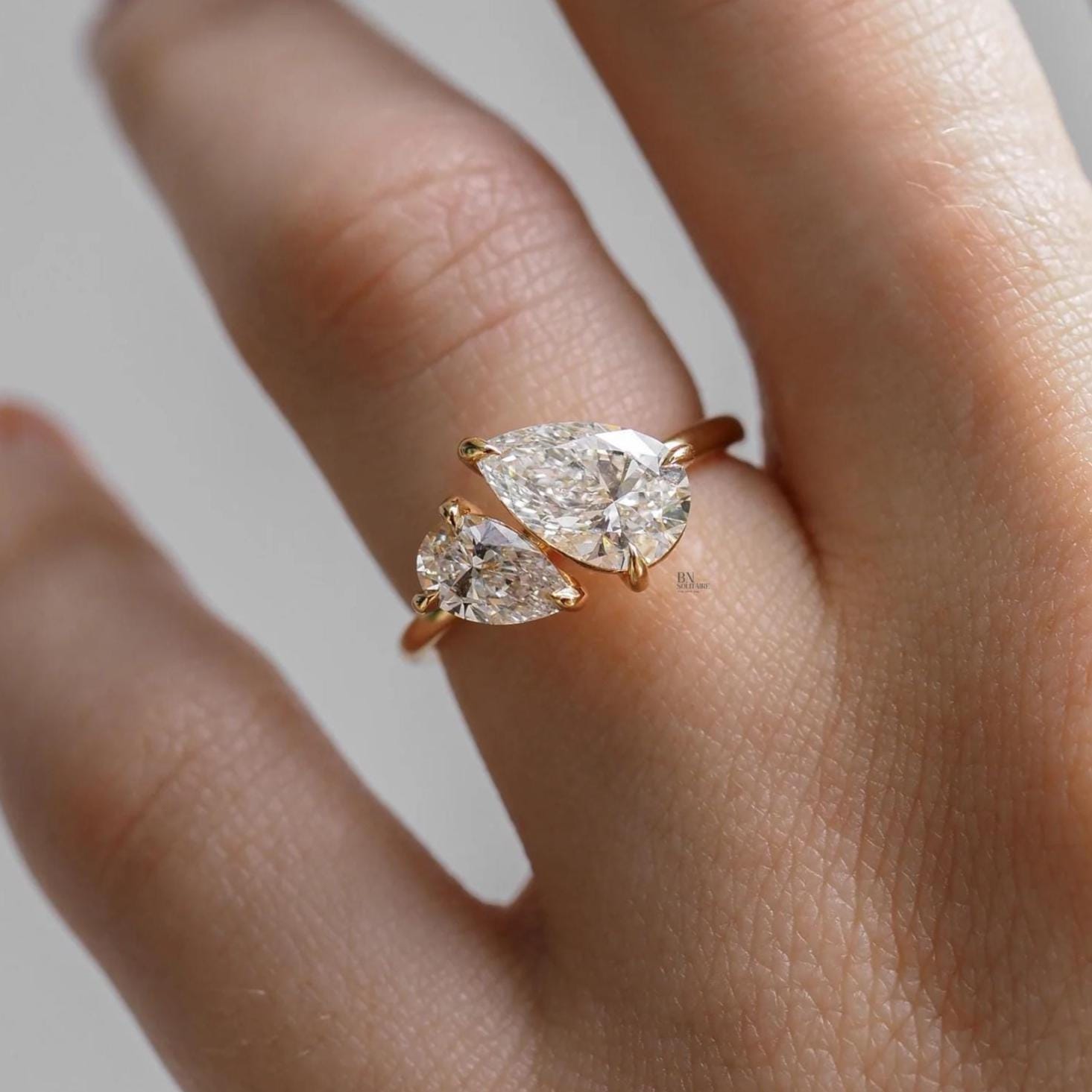 Close-up of 1 carat Pear Cut Lab Grown Diamond Toi et Moi ring featuring two asymmetrical stones nestled together, set in 14K yellow gold on a dainty band.