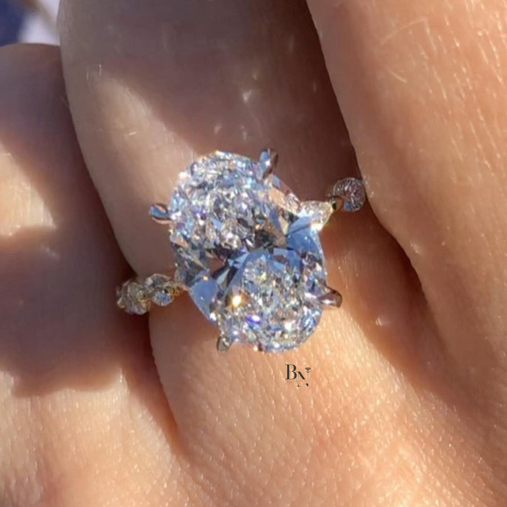 Hand shot of 3 carat oval cut lab grown diamond engagement ring in 14k yellow gold. Solitaire setting with unique marquise dot dash accent pave band. Brilliant cut stone shows maximum white light.