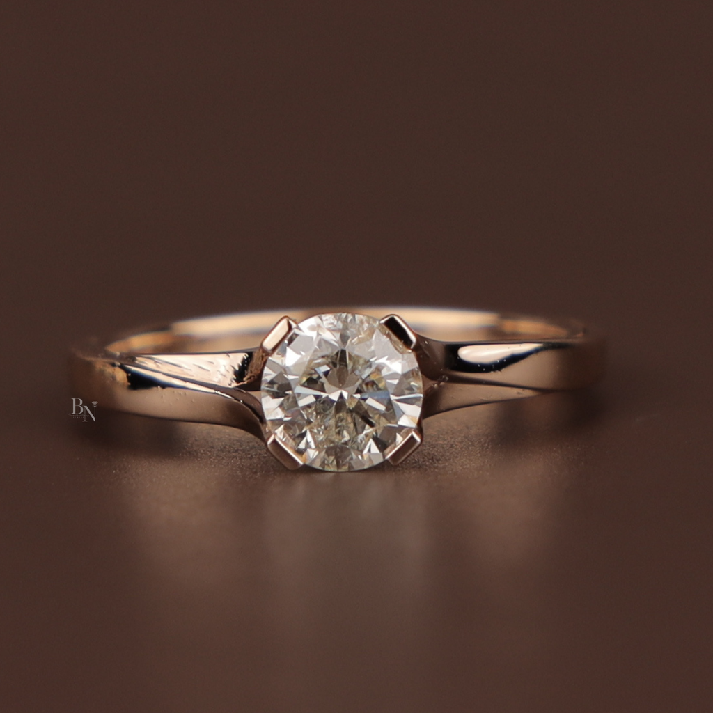 Bypass style engagement ring featuring a round brilliant cut lab grown diamond in a 14k yellow gold tension-inspired setting with a polished overlapping band held between fingers with red metallic nails.